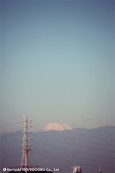 ビルの谷間の鉄塔の向こうに富士山の頭が見えている